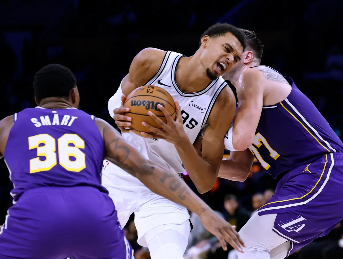 0x0 | GGSLOT | Sports & Games News Basketball player in white aggressively drives with the ball while two defenders in purple Lakers jerseys guard him.",
