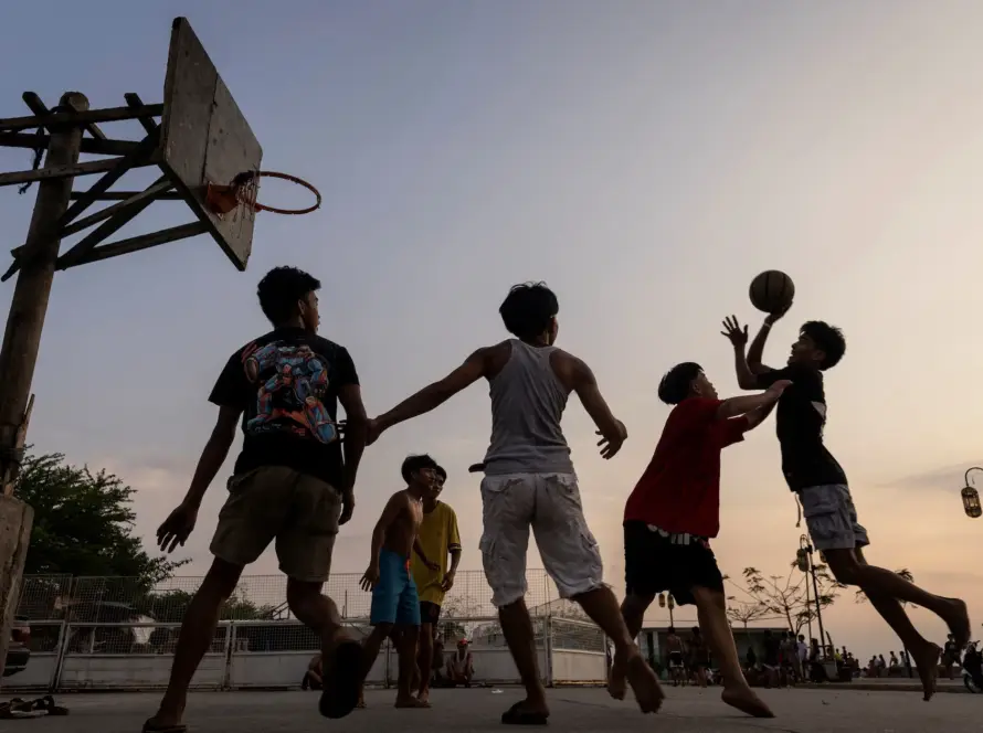 Alt Text: Community members playing Filipino Street Ball on an outdoor neighborhood court during sunset.