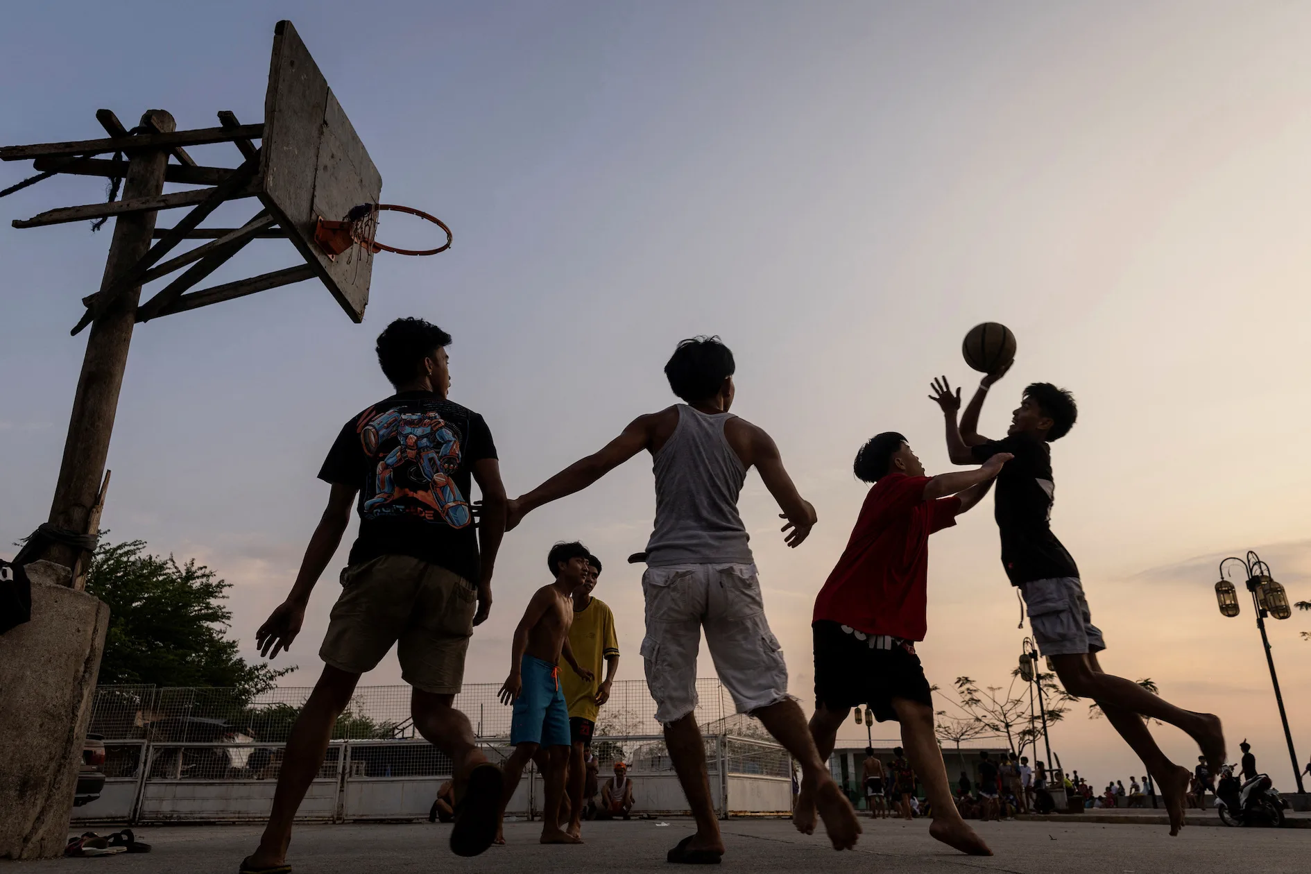 Community members playing Filipino Street Ball | GGSLOT | Sports & Games News Alt Text: Community members playing Filipino Street Ball on an outdoor neighborhood court during sunset.