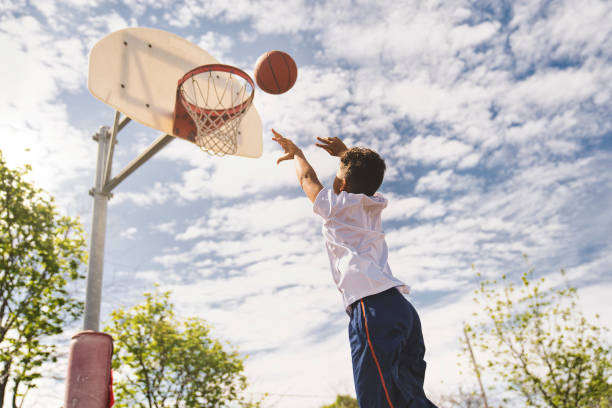 A nice and cool Afro american players playing basketball outdoors | GGSLOT | Sports & Games News A young boy reaching up at a basketball hoop with determination.