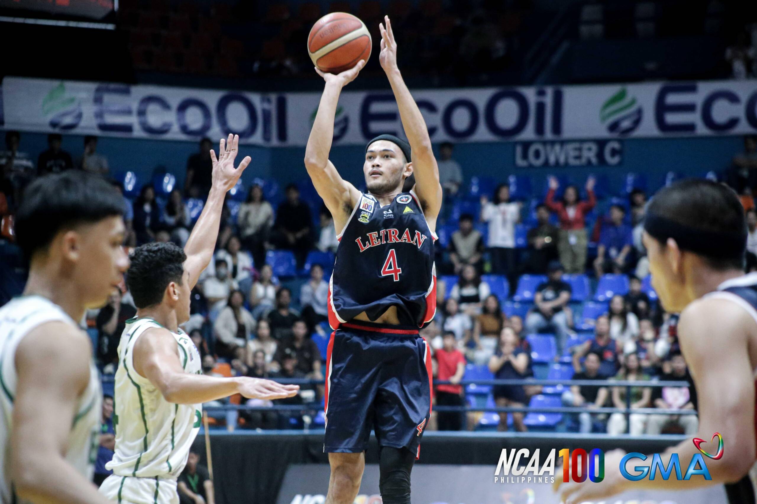 letran-knights-basketball-kevin-santos-defense | GGSLOT | Sports & Games News Kevin Santos jumps to take a jump shot as defenders contest the shot in a crowded arena.