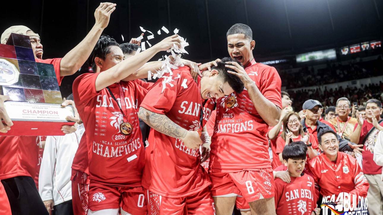 Basketball players in red uniforms celebrate a championship on the court as confetti swirls around them.