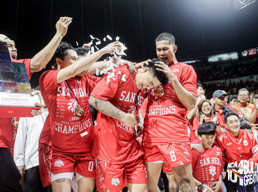 Basketball players in red uniforms celebrate a championship on the court as confetti swirls around them.