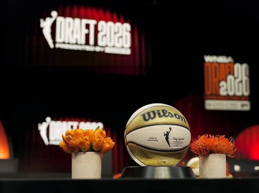 Wilson basketball on a display pedestal on a stage, flanked by orange flowers, with a 'DRAFT 2026' banner in the background.