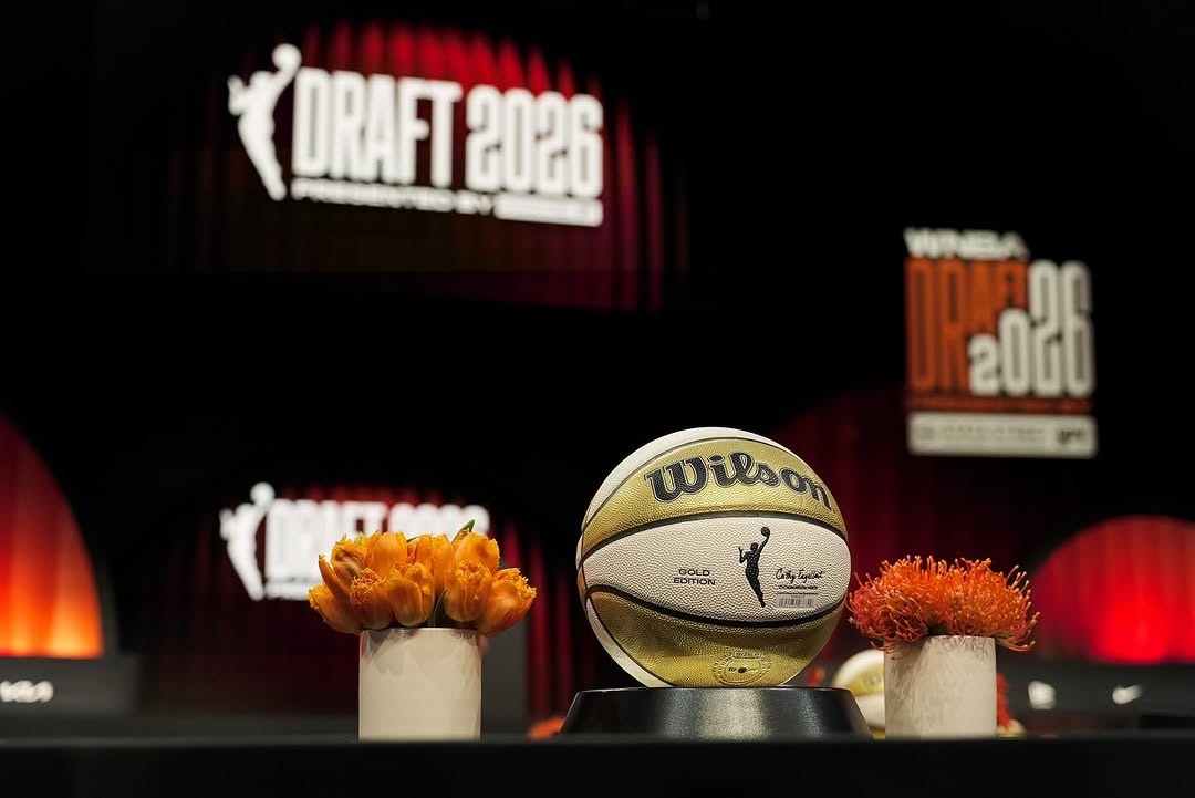 Wilson basketball on a display pedestal on a stage, flanked by orange flowers, with a 'DRAFT 2026' banner in the background.