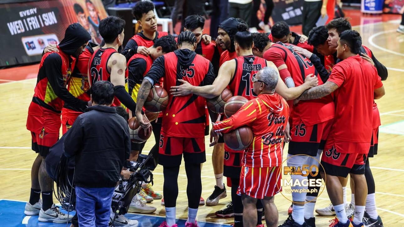 Basketball team in red uniforms huddling in a circle on the court during a timeout or team talk.
