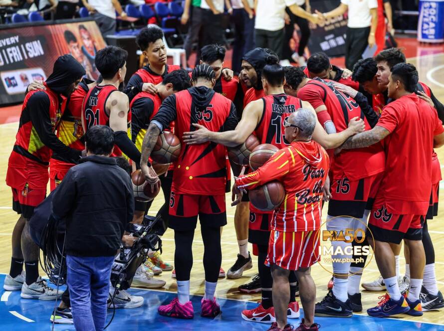 Basketball team in red uniforms huddling in a circle on the court during a timeout or team talk.