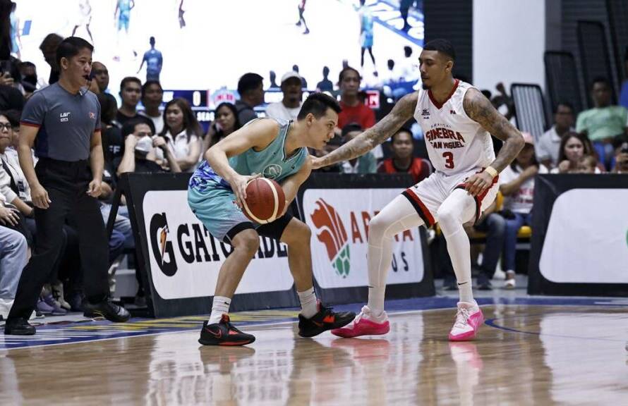 Basketball player in a teal jersey drives with the ball past a defender in a white jersey (number 3) on a crowded indoor court with spectators watching.