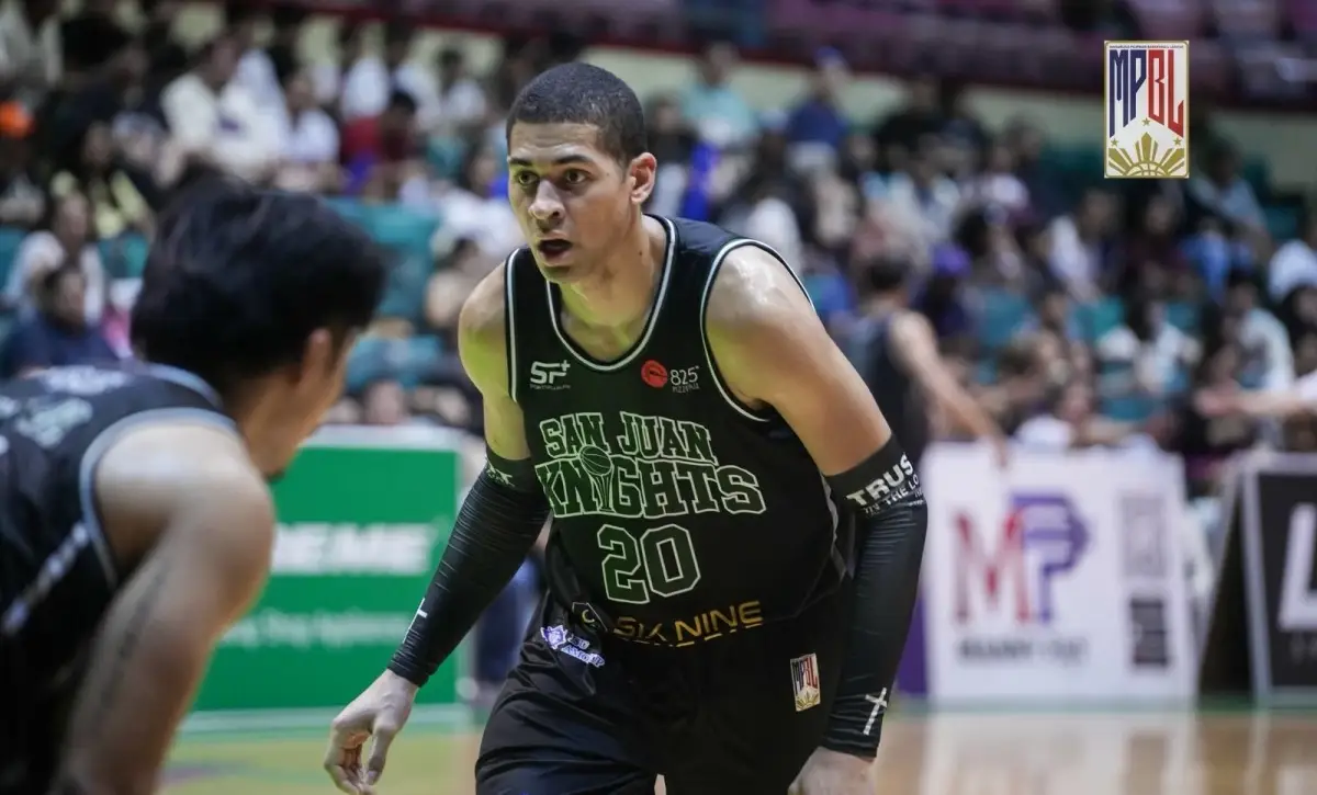 Basketball player wearing San Juan Knights jersey #20 guards the opponent on a court with a crowd in the background