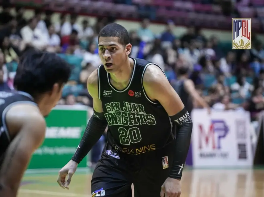 Basketball player wearing San Juan Knights jersey #20 guards the opponent on a court with a crowd in the background
