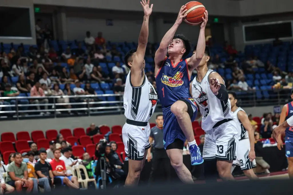 A Rain or Shine Elasto Painters player in a blue jersey drives for a layup while being defended by two Blackwater Bossing players in white jerseys during a PBA basketball game.