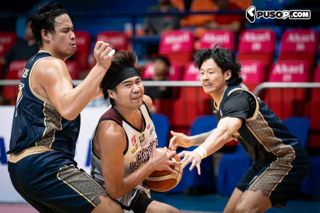 Basketball player in white attempts to drive with the ball while two defenders reach in from the sides in a crowded court scene.