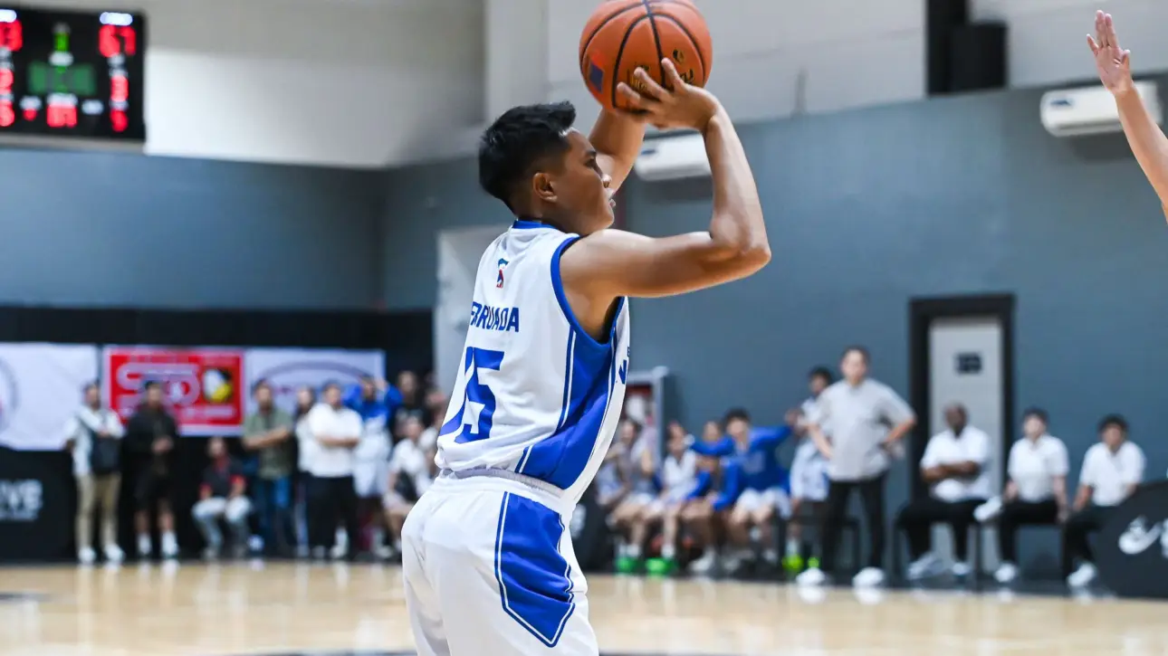 Basketball player in a white and blue uniform shooting a ball during a game, blurred spectators in the background.