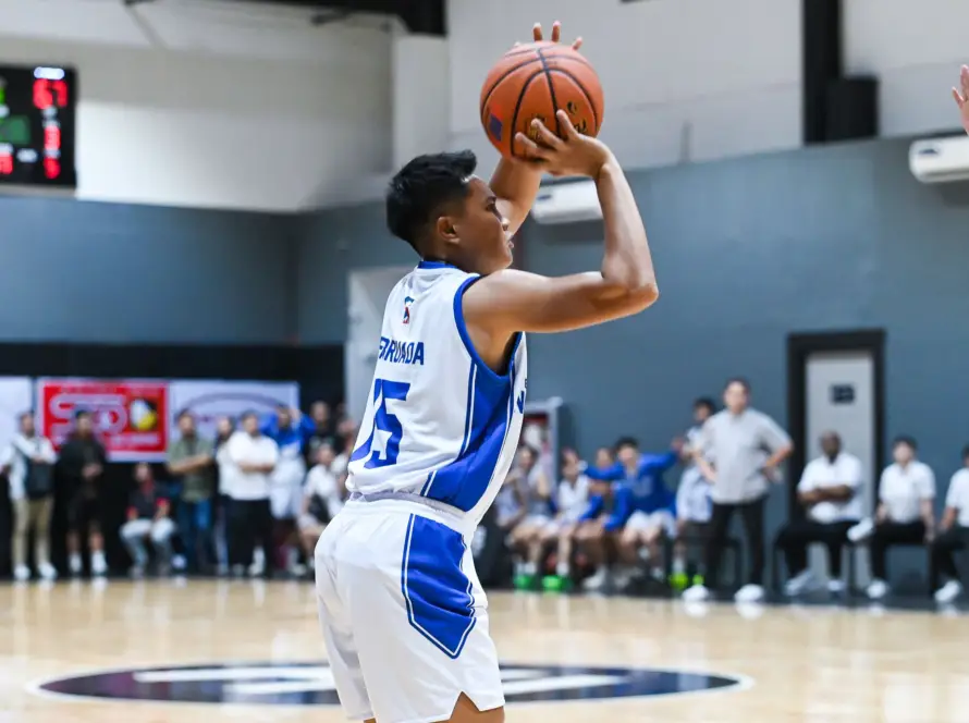 Basketball player in a white and blue uniform shooting a ball during a game, blurred spectators in the background.