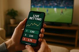 A mobile smartphone displaying live sports betting lines handicap spreads and future win total projections | GGSLOT | Sports & Games News Hand holding a smartphone showing live betting odds (e.g., 2.60, 3.10, 2.75) with a football match on TV in the background