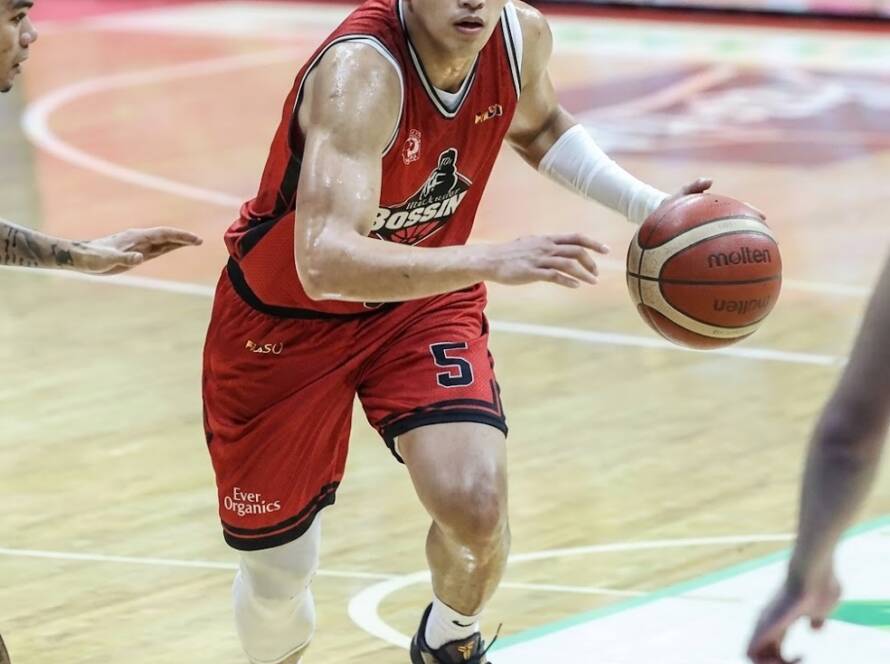 Basketball player in red jersey number 5 dribbles down the court, focused, left arm extended, indoors arena.