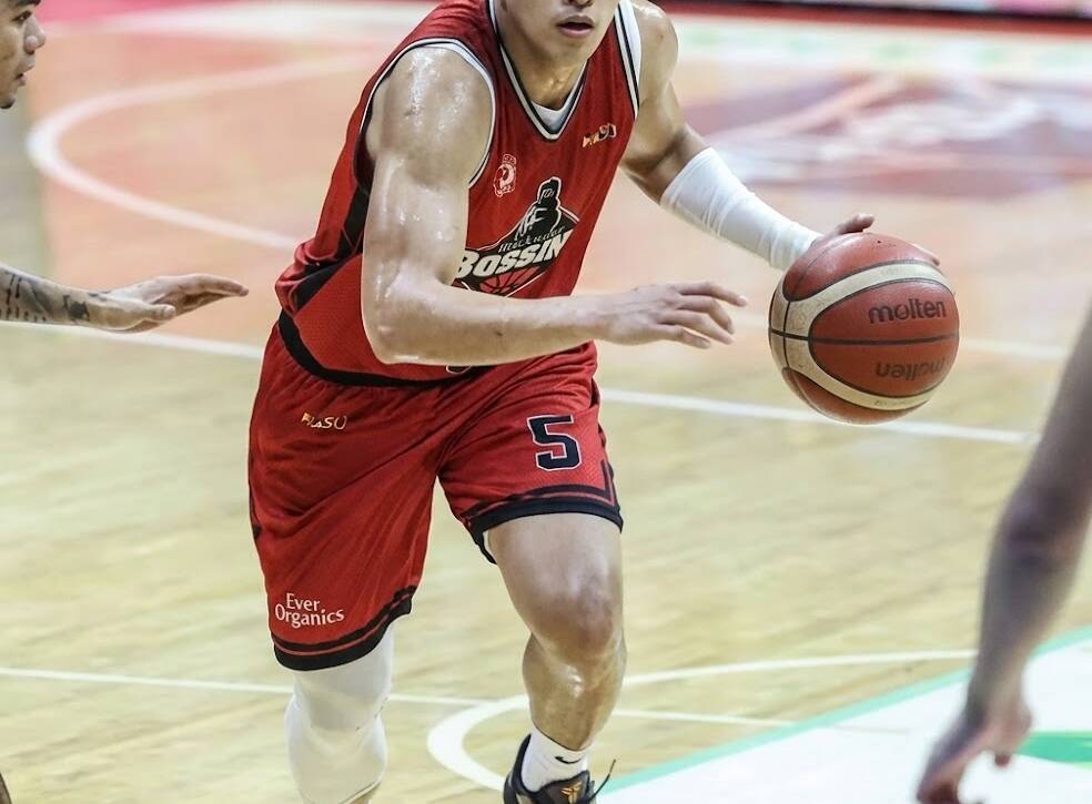 Basketball player in red jersey number 5 dribbles down the court, focused, left arm extended, indoors arena.