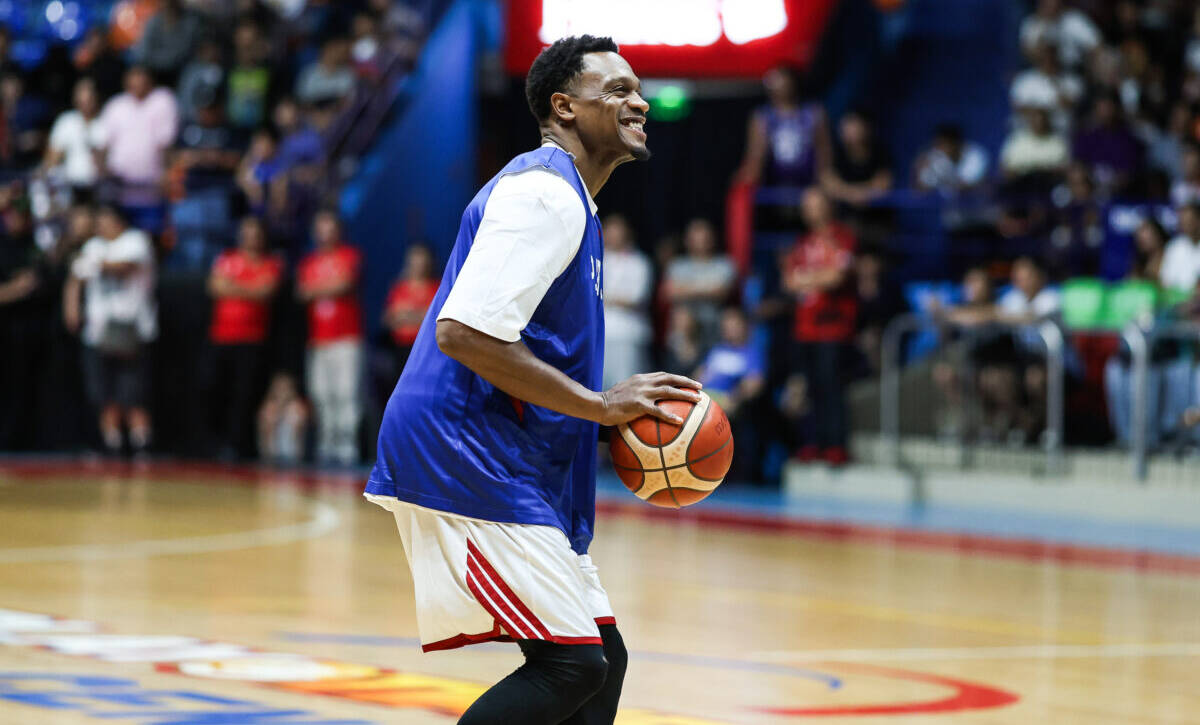 Basketball player in a blue jersey dribbles a ball on a gym court with cheering crowd in the background