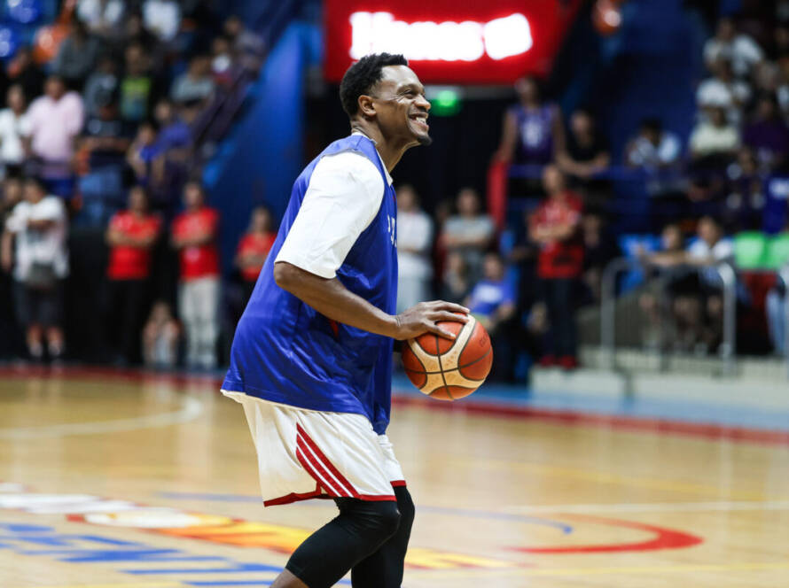 Basketball player in a blue jersey dribbles a ball on a gym court with cheering crowd in the background
