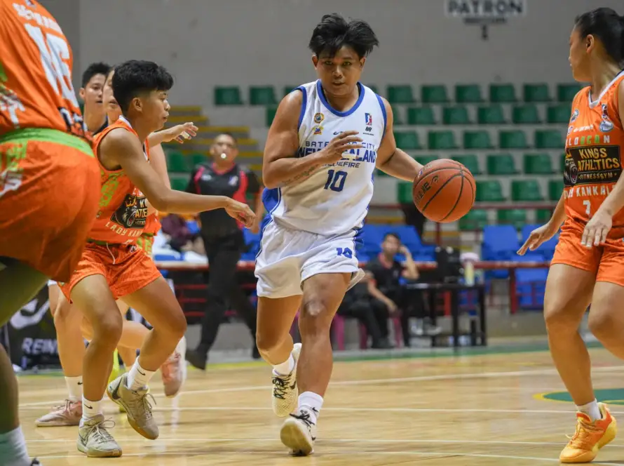 White-jersey player (number 10) dribbles toward the basket while orange-team defenders converge in a crowded, indoor basketball game.