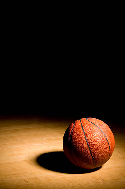 nba-draft-betting-tips-rookie-odds | GGSLOT | Sports & Games News A high-resolution close-up of a professional basketball resting on a polished indoor hardwood court floor with reflective stadium lights