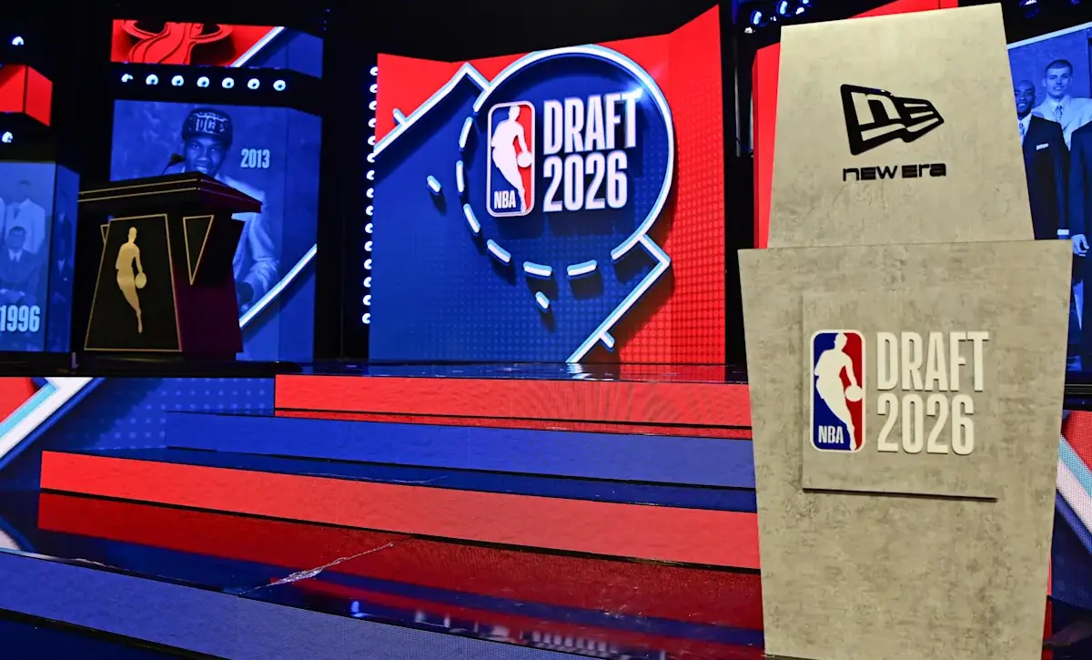 Stage setup for NBA Draft 2026 with red and blue steps leading to a large screen reading DRAFT 2026 and a beige podium featuring a New Era logo.