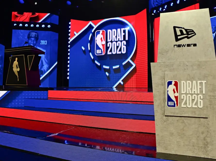Stage setup for NBA Draft 2026 with red and blue steps leading to a large screen reading DRAFT 2026 and a beige podium featuring a New Era logo.