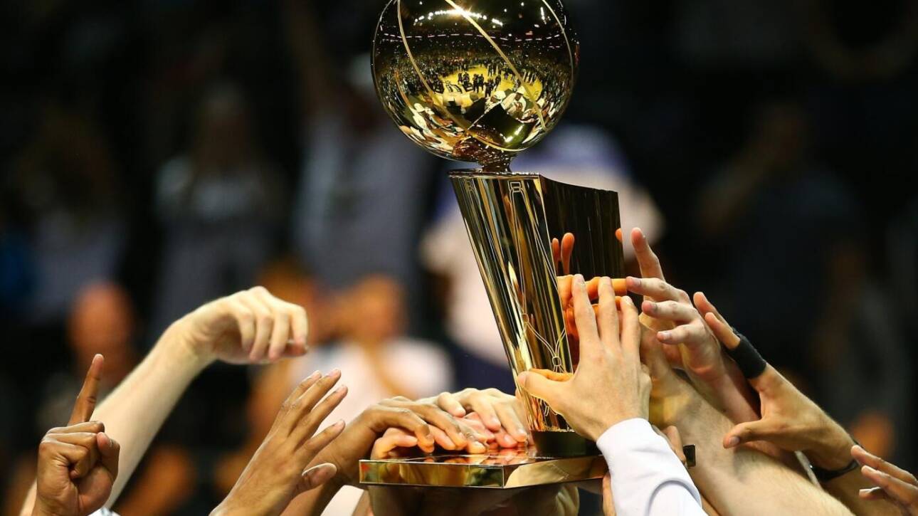A group of hands lifting a shiny sports trophy together in celebration.