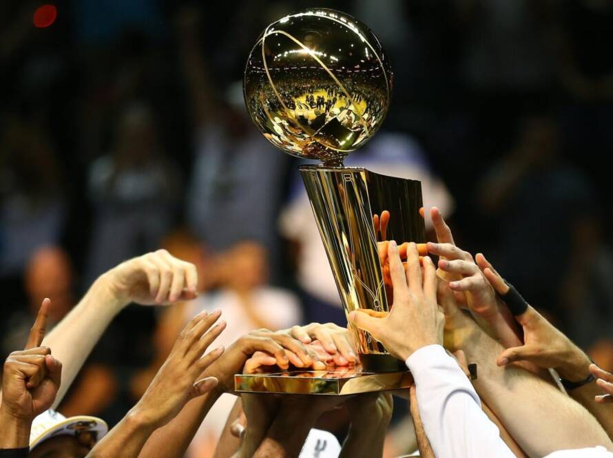 A group of hands lifting a shiny sports trophy together in celebration.