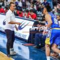 Basketball coach shouting at a blue-and-yellow team player near the bench during a game.