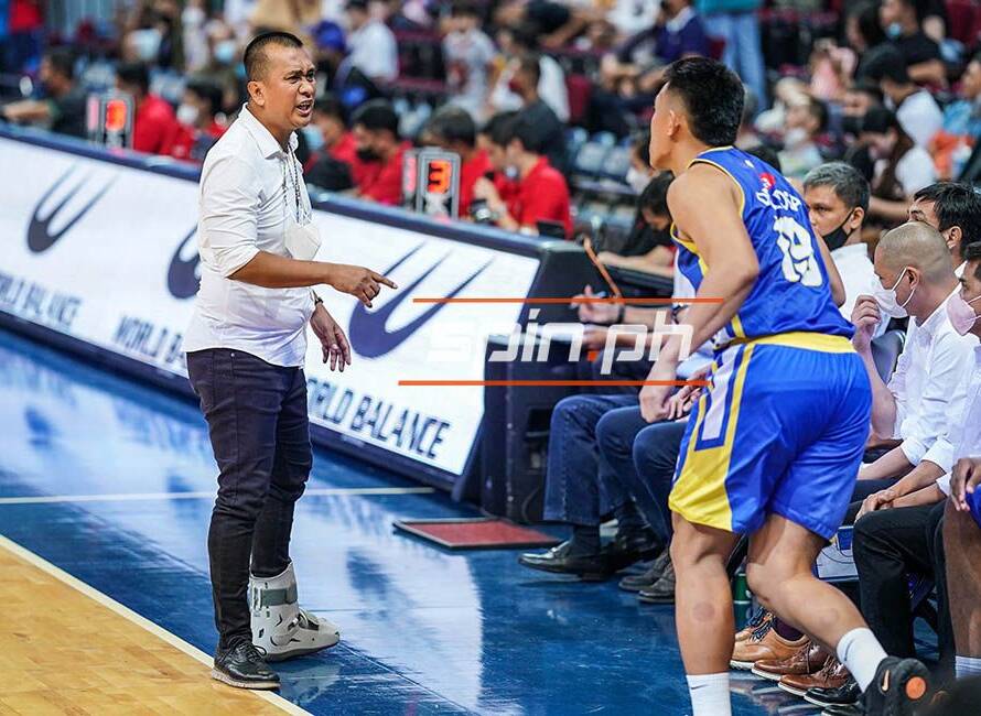 Basketball coach shouting at a blue-and-yellow team player near the bench during a game.