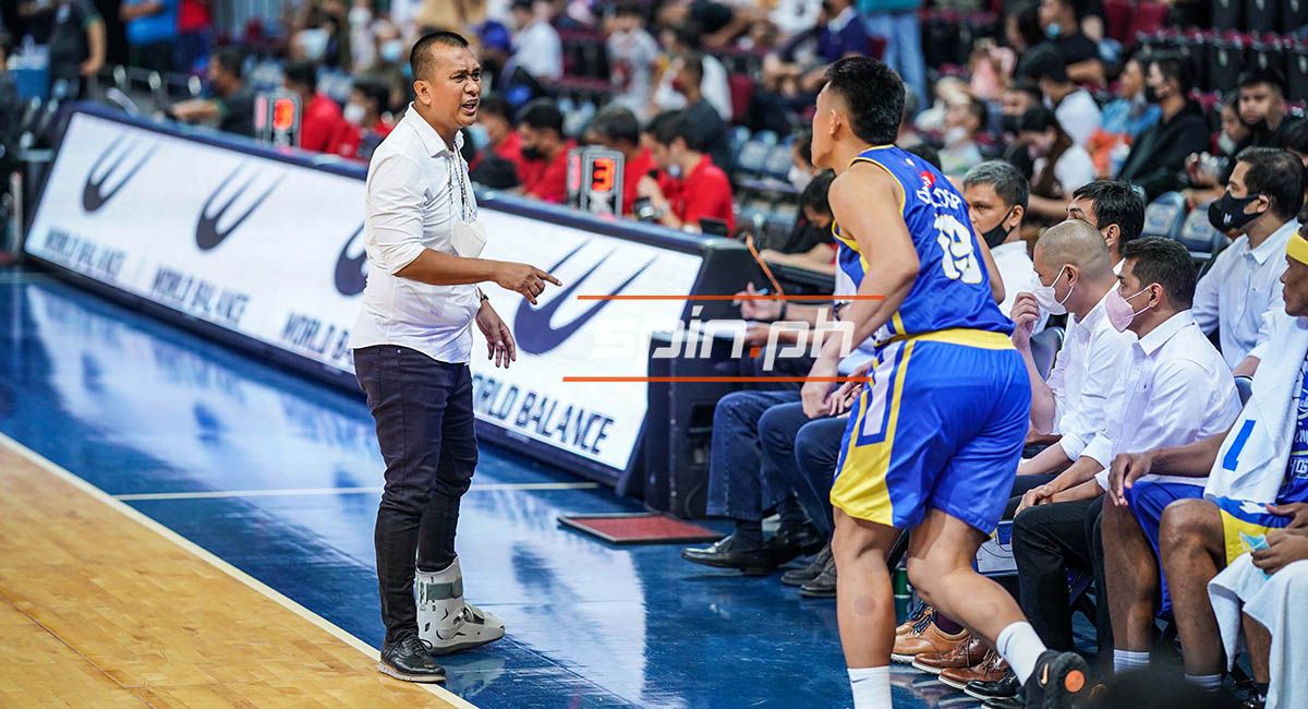 Basketball coach shouting at a blue-and-yellow team player near the bench during a game.