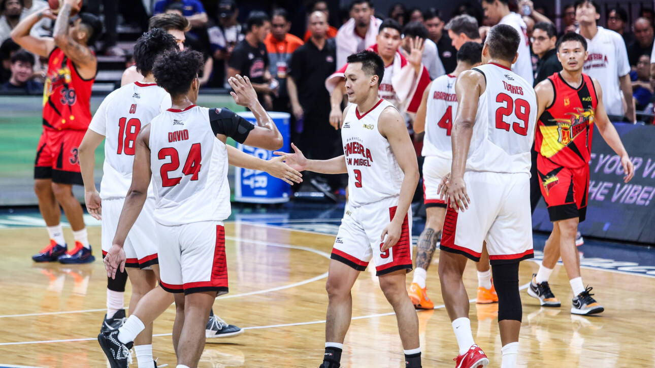 Basketball players in white and red jerseys high-fiving on a court after a game, with spectators in the stands behind them.
