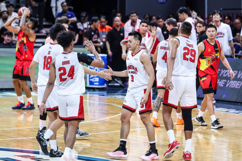 Basketball players in white and red jerseys high-fiving on a court after a game, with spectators in the stands behind them.