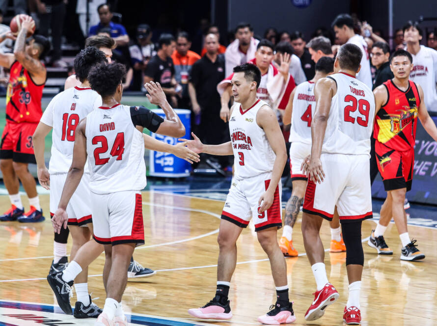 Basketball players in white and red jerseys high-fiving on a court after a game, with spectators in the stands behind them.