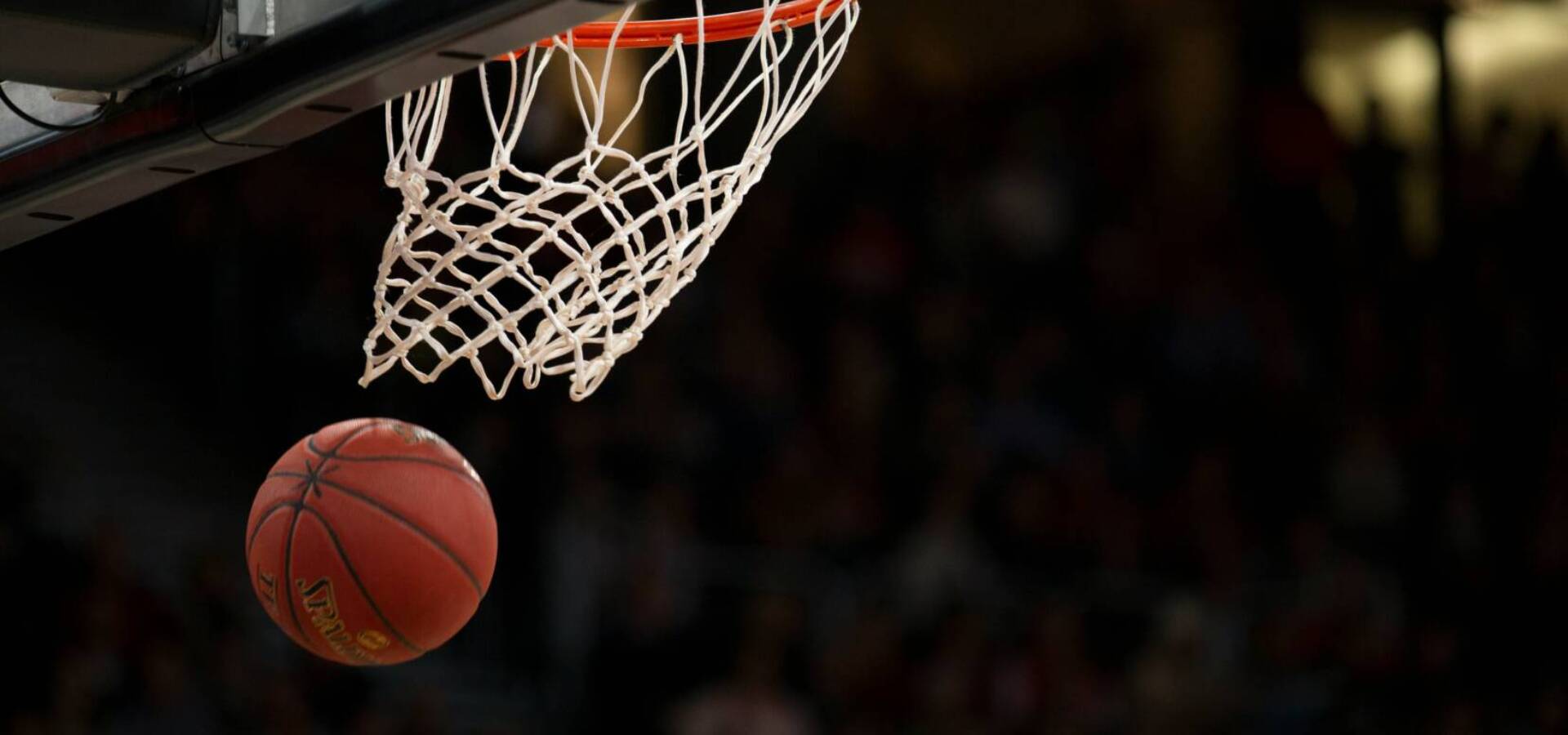 close-up-pba-basketball-ball-hoop | GGSLOT | Sports & Games News Detailed close-up shot of a basketball swirling into a net with professional arena lights and banners blurred in the background.