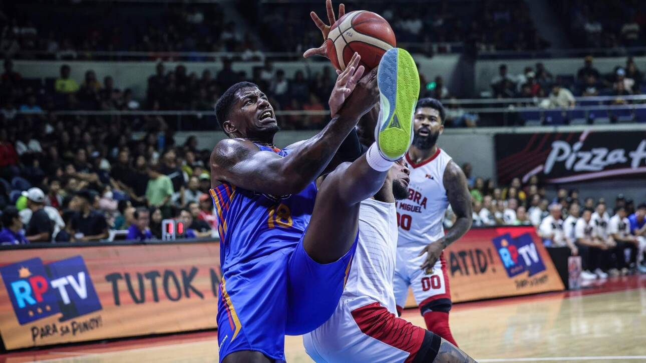 Two players leap for the basketball in a crowded indoor arena during a high-energy game.