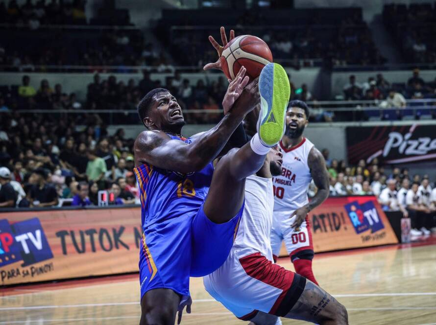 Two players leap for the basketball in a crowded indoor arena during a high-energy game.