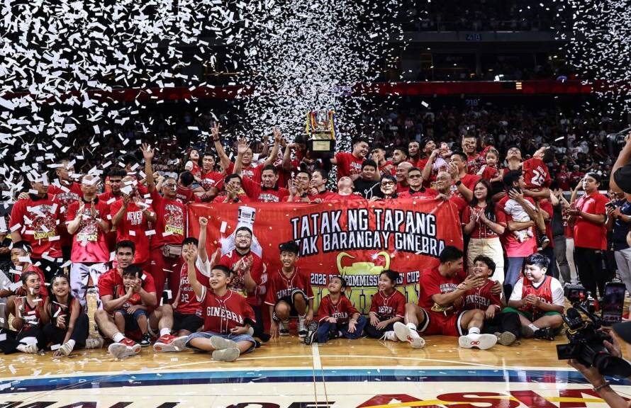 Basketball team and fans in red celebrate on court with a trophy and confetti filling the arena.