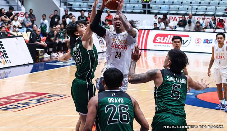 White Ultras player #24 drives to the hoop while green-team defenders contest the shot near the basket, crowd watching in the stands.